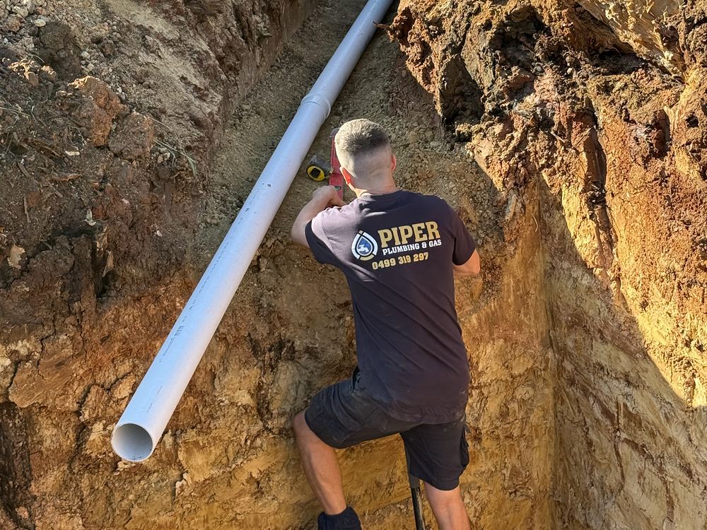 Craig laying a new PVC sewer line at the bottom of a deep trench